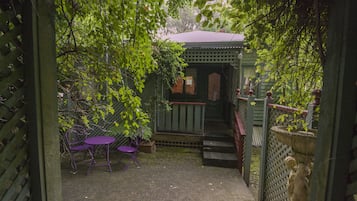 A covered outdoor seating area with a table and chairs, a small wooden structure, and a statue.