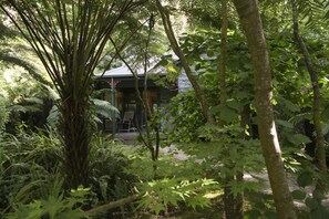 A building surrounded by dense greenery, including ferns and trees, with a visible entrance and seating area. - Cottages at Monreale (Olinda)