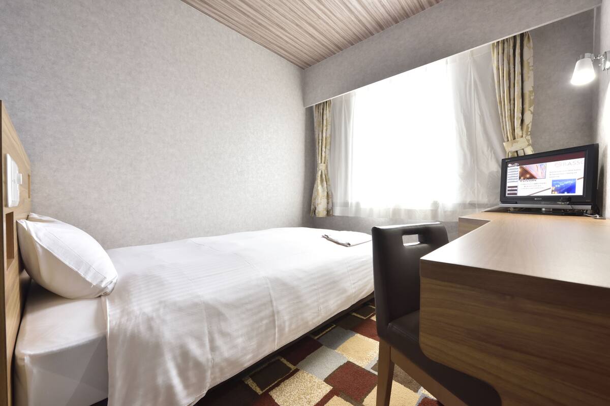 Ett hotellrum med en säng, ett skrivbord med en dator och ett fönster med gardiner.