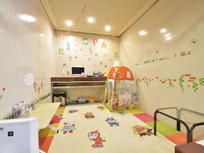 Una sala de juegos infantiles con un letrero 'KIDSPARK', tapetes de juego coloridos y una tienda de campaña.