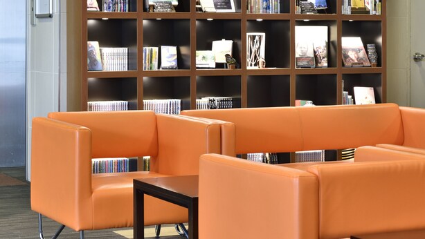 Una biblioteca con asientos naranjas y una estantería grande.