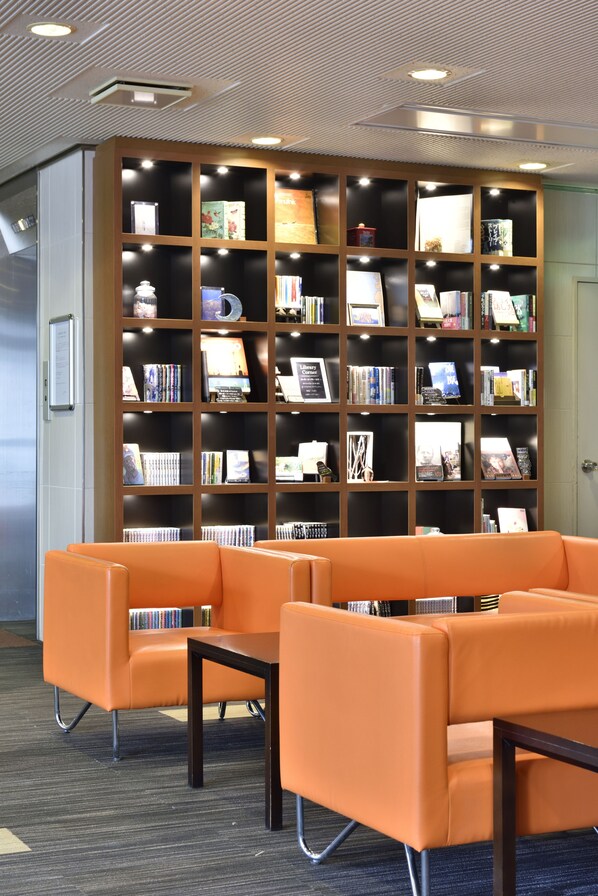 A library with orange seating and a large bookshelf. - Hotel WBF Kushiro (Kushiro)