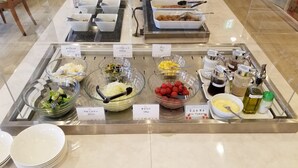 Buffet amb plats identificats incloent bròcoli, col i tomàquets petits.