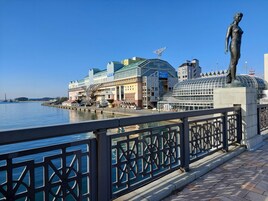 Un paseo marítimo con una estatua, edificios modernos y cielo despejado.