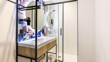 A modern bathroom with a glass shower enclosure, a wooden vanity with a sink, and a large mirror.
