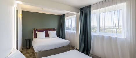 A hotel room with two beds, a view of the city, and a window with sheer curtains.
