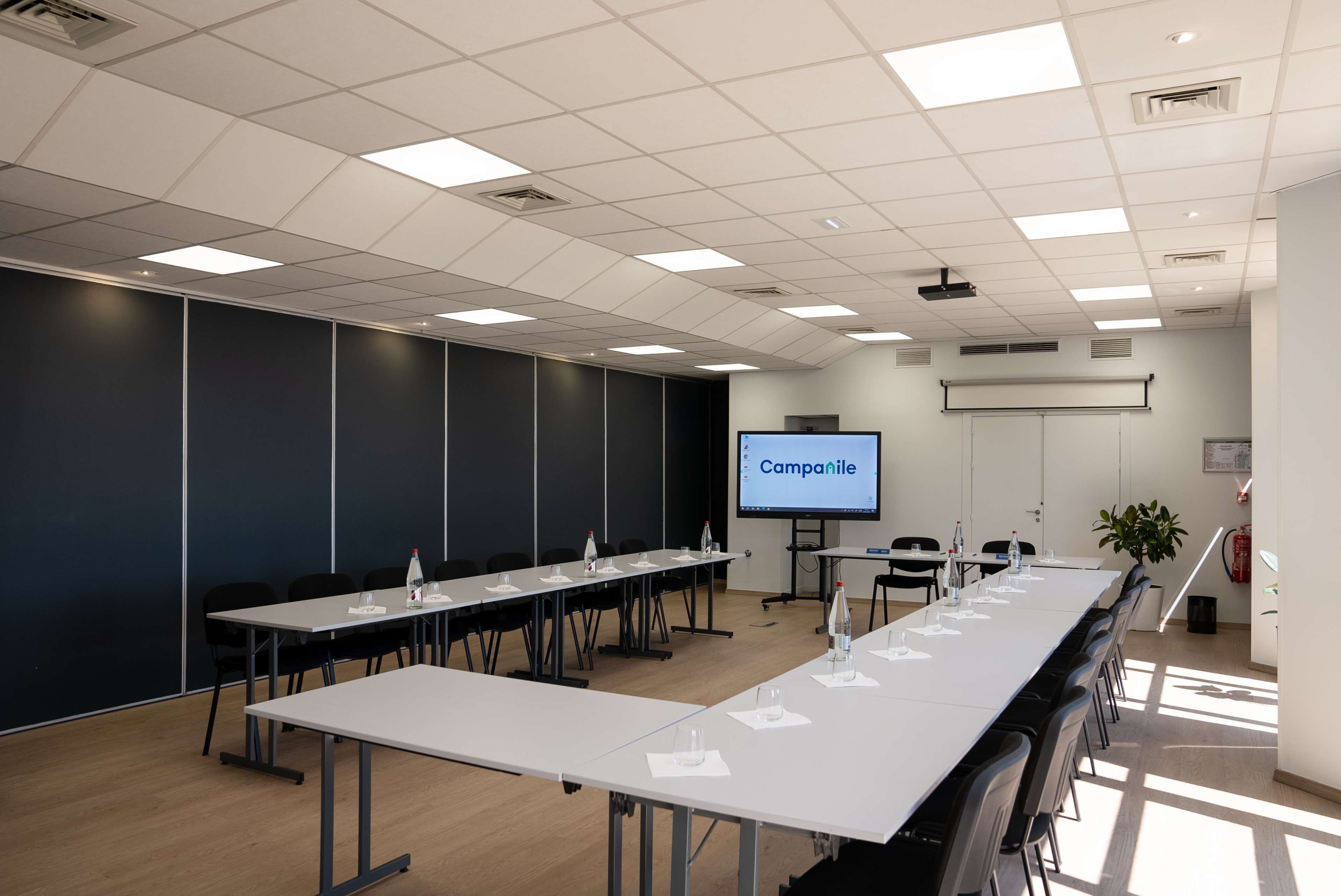 Ein Konferenzraum mit einem langen Tisch, Stühlen, einer Projektionsleinwand und einem Präsentationsbildschirm, der "Campanile" zeigt.