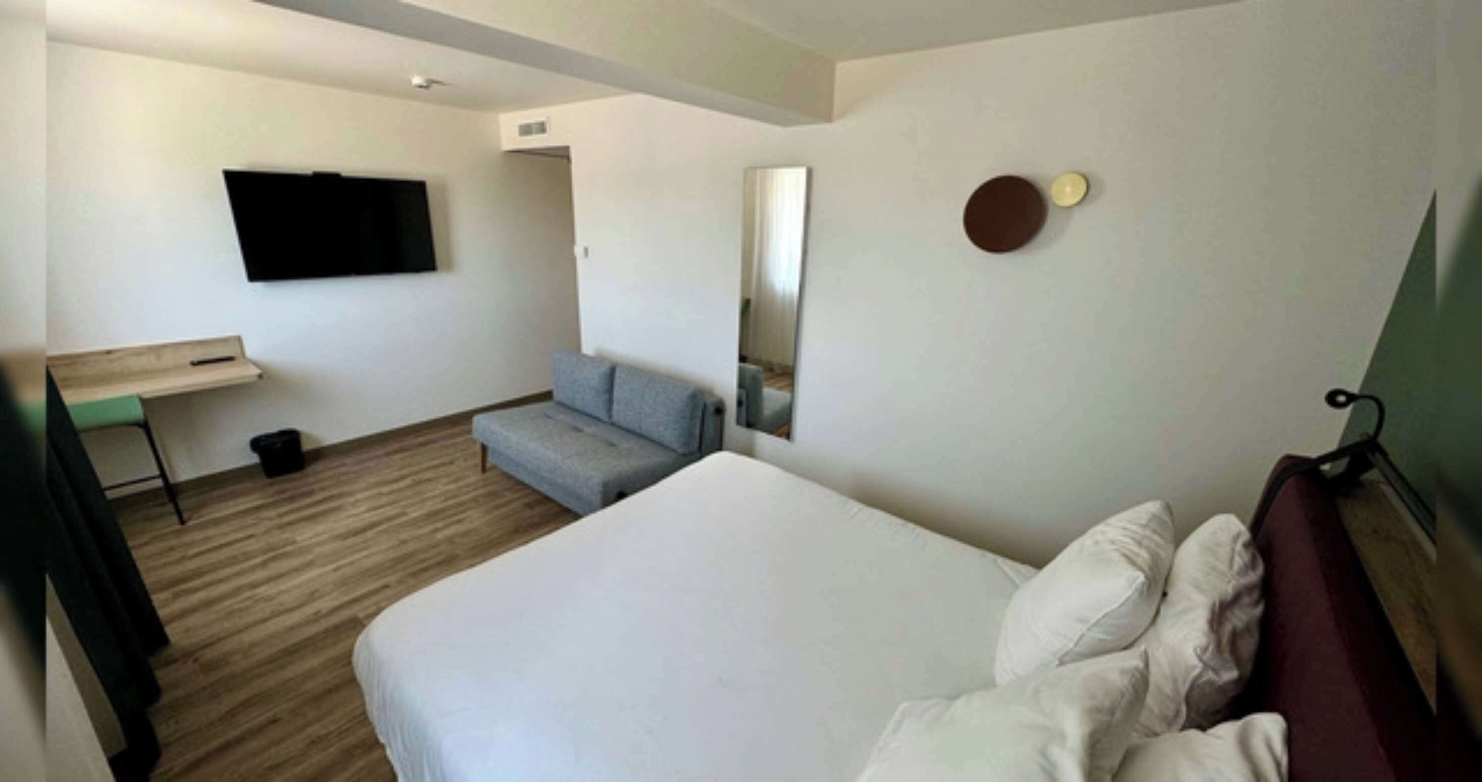 A hotel room with a bed, a desk, a chair, a television, and a mirror.