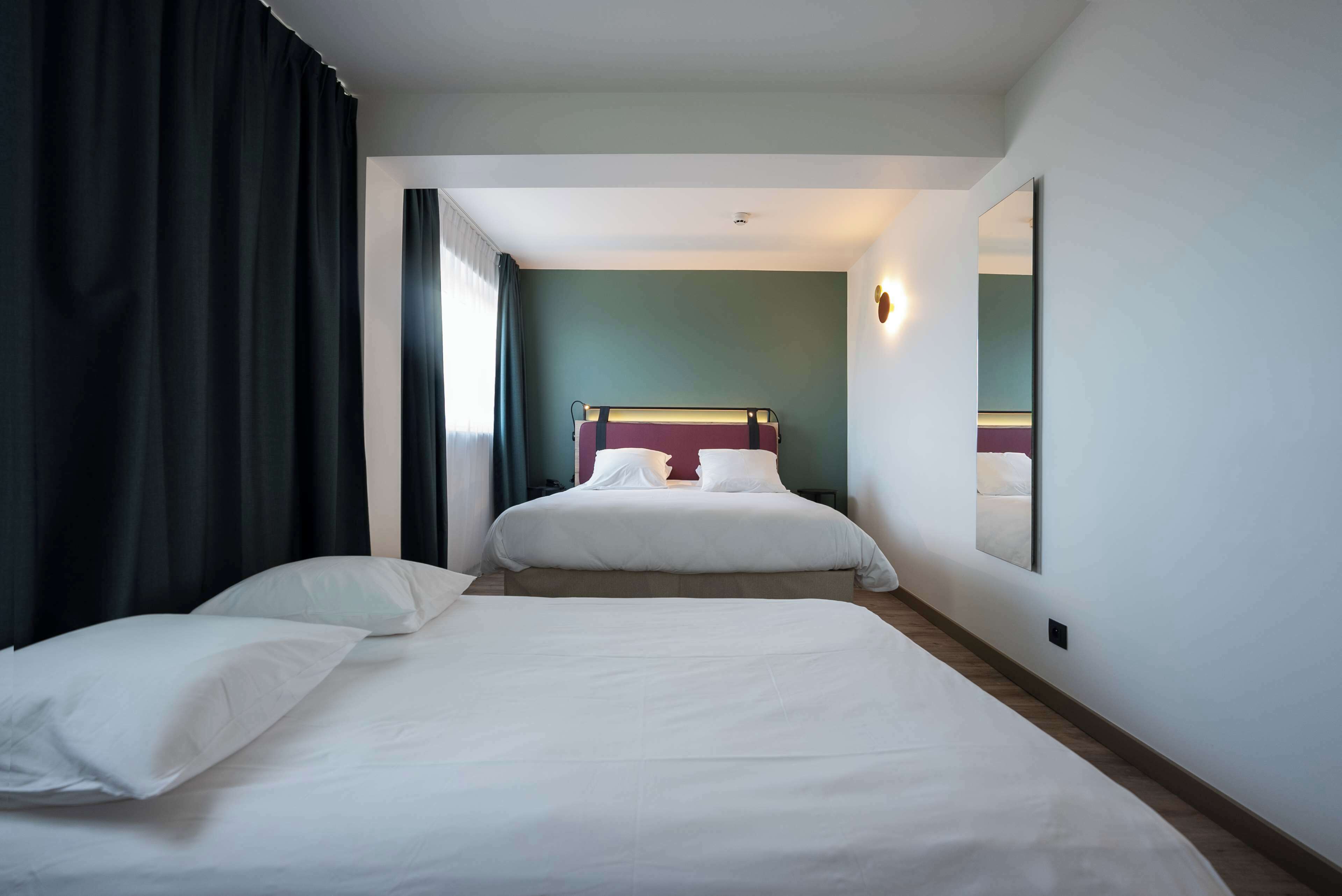 Ein Hotelzimmer mit zwei Betten, einem großen Spiegel und Blick auf den Flur.