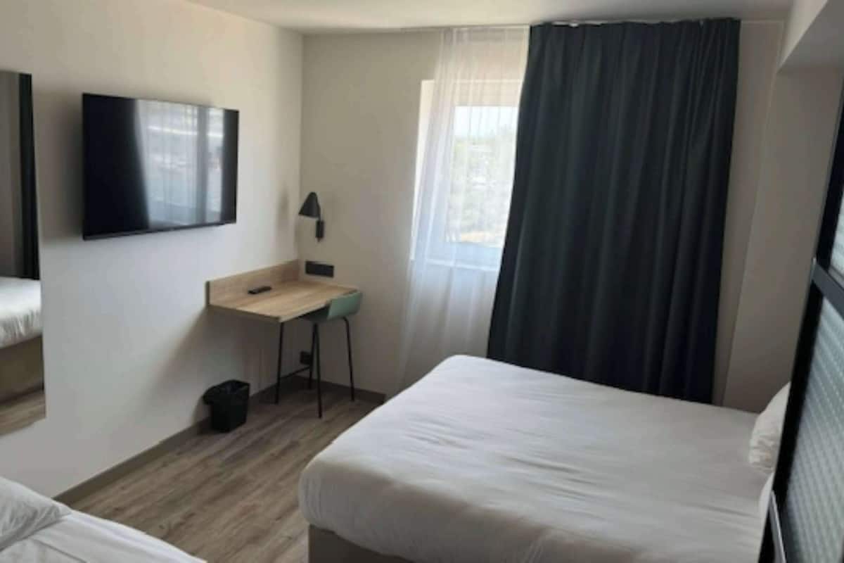 Een hotelkamer met twee bedden, een bureau, een stoel, een televisie en een raam met gordijnen.
