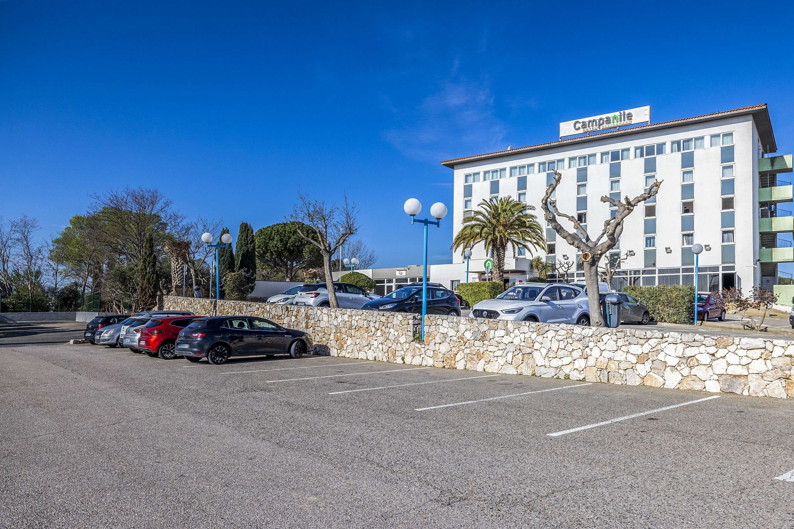 Hotel com área de estacionamento com parede de pedra e céu azul límpido.
