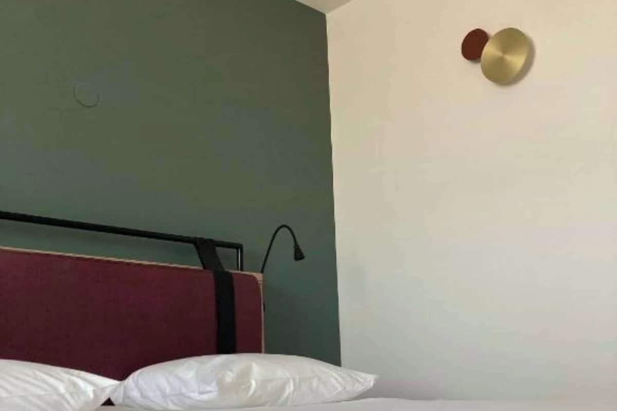 Een opgemaakt bed met witte lakens in een kamer met een groene accentmuur en een eenvoudig, modern hoofdbord.