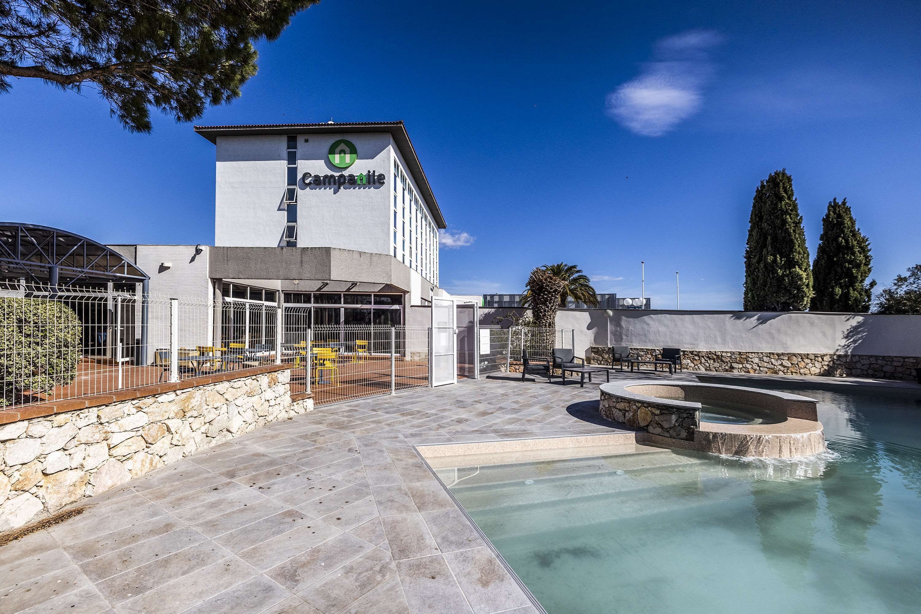 Un hotel con zona de piscina, paredes de piedra y un edificio con un cartel.