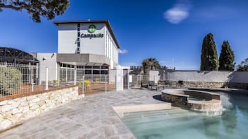 Un hotel con zona de piscina, paredes de piedra y un edificio con un cartel.