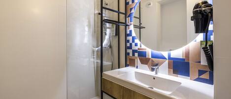 A modern bathroom with a glass shower enclosure, a white sink, and a mirror with a geometric tile backsplash.