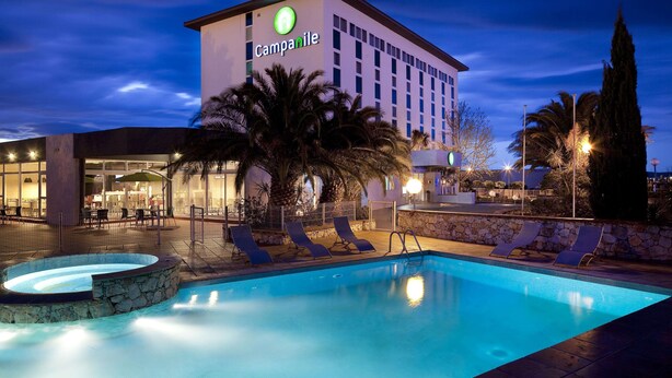 Un hotel con piscina, sillas de descanso y palmeras.