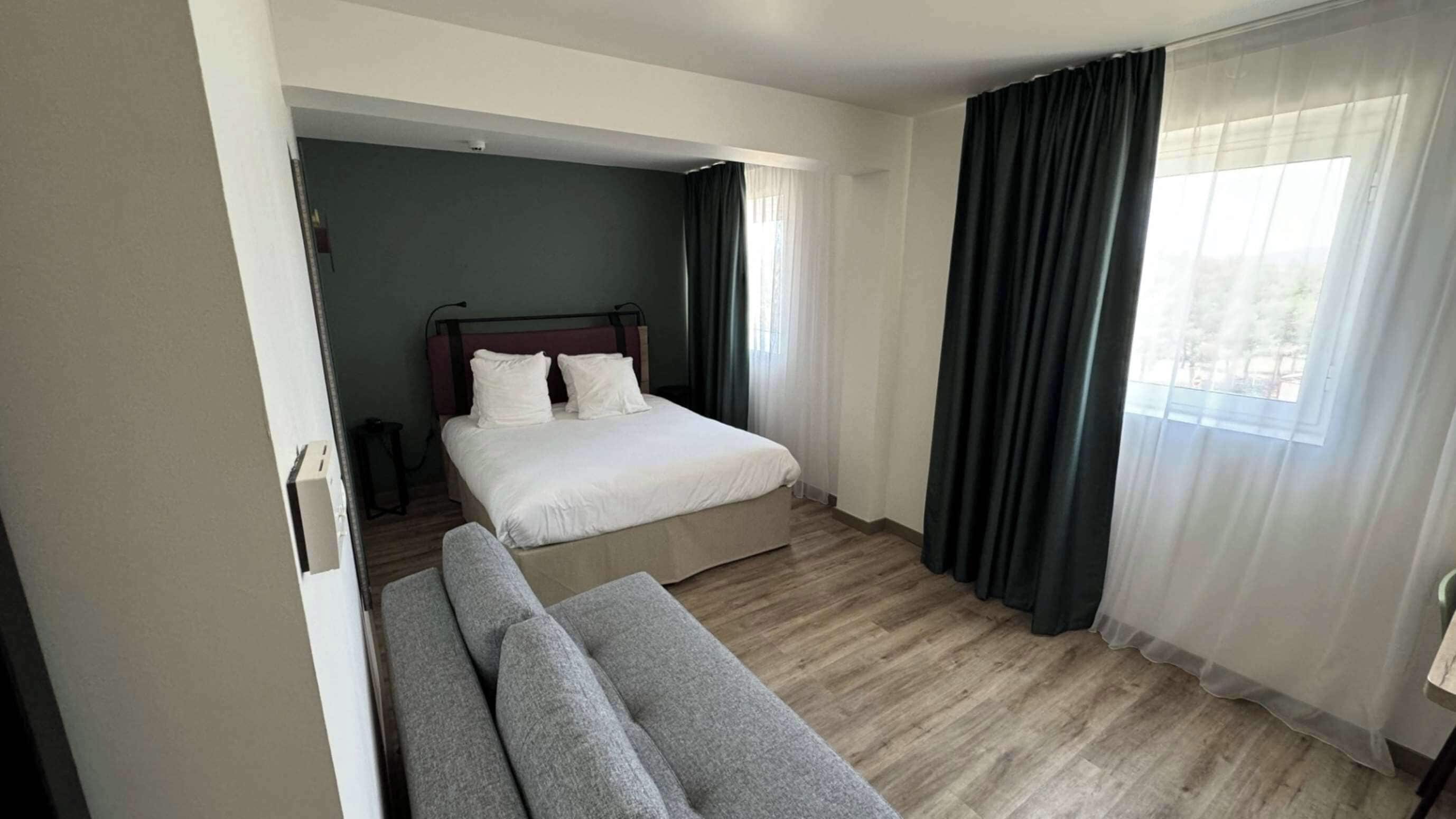 A modern hotel room with a bed, a sofa, and a view of the outdoors.