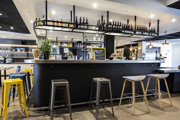Un área de bar moderna con una barra curva, varios taburetes y una selección de botellas exhibidas en estantes.