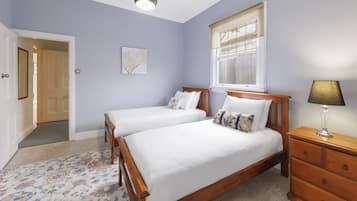 Un dormitorio con dos camas de madera, una mesita de noche, una lámpara, una ventana con persianas, una puerta y suelo alfombrado.