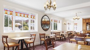 A dining area with multiple wooden tables and chairs, large windows with stained glass, and a chandelier. - Hotel Blue & Cottages, Katoomba (Katoomba)