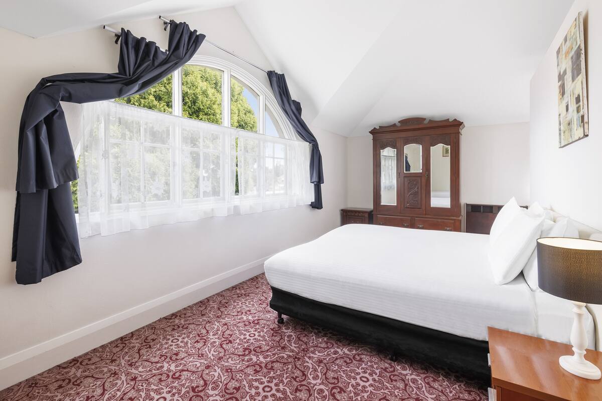 A bedroom with a large bed, a wooden wardrobe, and a window with curtains.