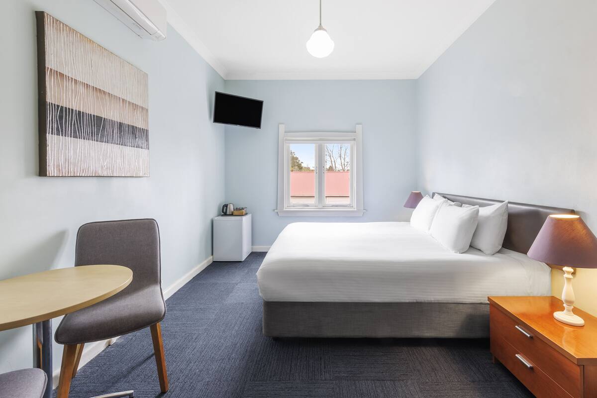 A hotel room with a bed, a desk, a chair, a TV, and a window.