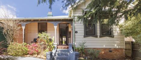 A two-story house with a front porch, a brick foundation, and a well-maintained garden.