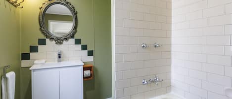 Un baño con lavamanos blanco, espejo y bañera. Hay un toallero y un jabonera en el lavamanos.