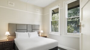 A neatly made bed with a headboard, two bedside lamps, and a window with a view of trees. - Hotel Blue & Cottages, Katoomba (Katoomba)