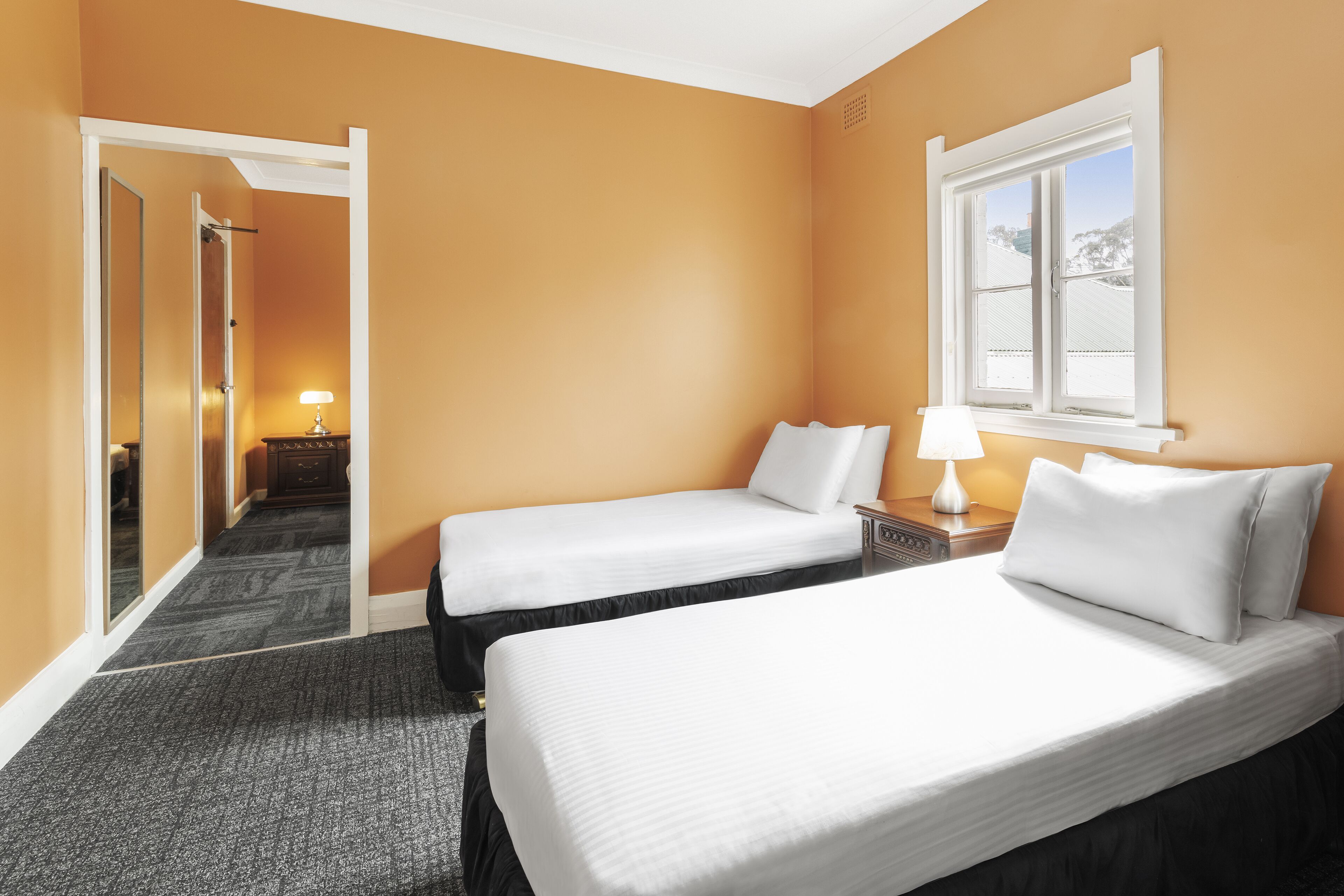 A hotel room with two beds, a window, a door, and a lamp.