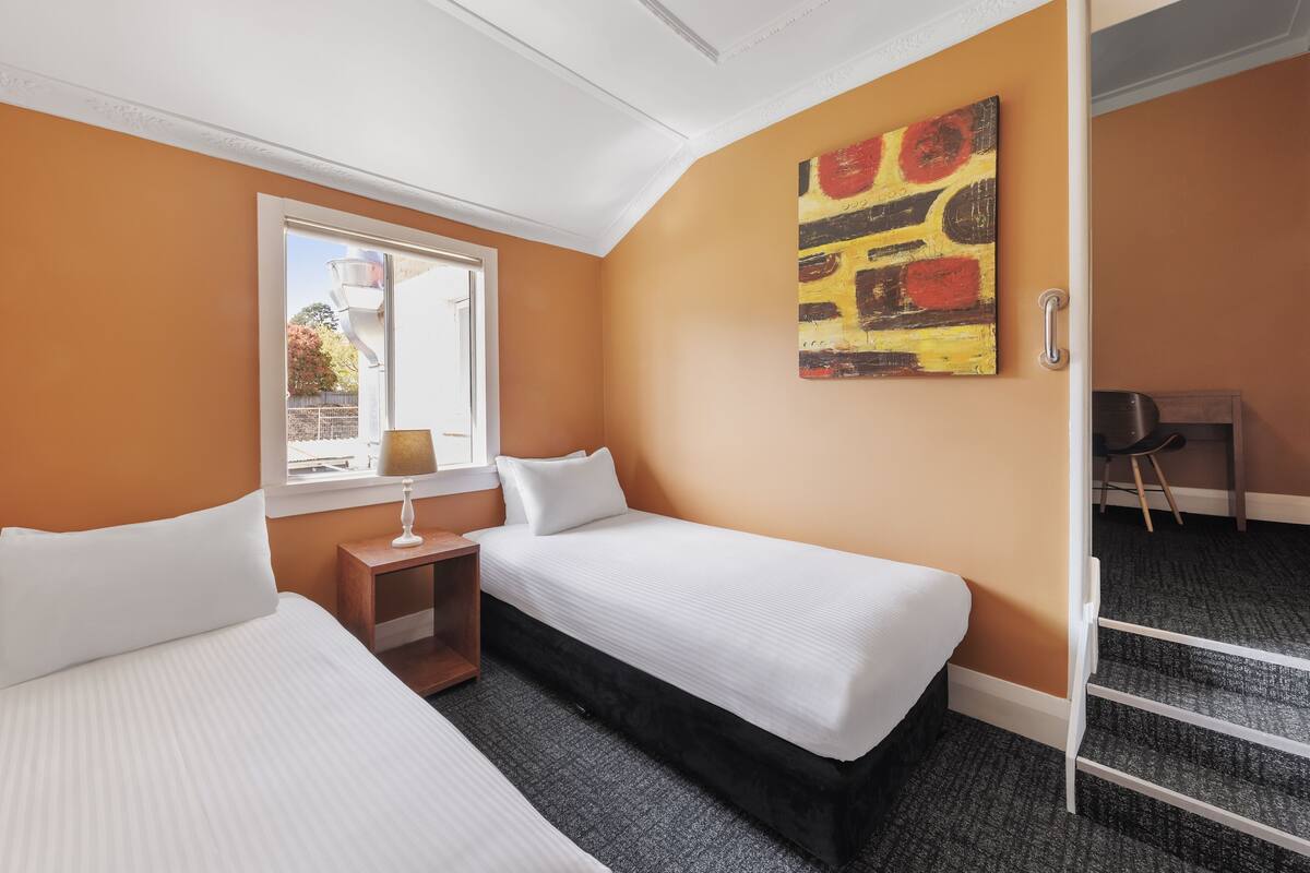 A hotel room with two beds, a window, a painting, and a desk.