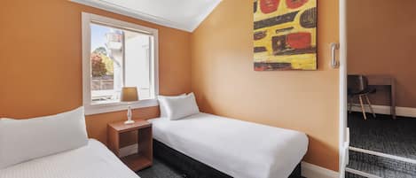 A hotel room with two beds, a window, a painting, and a desk.