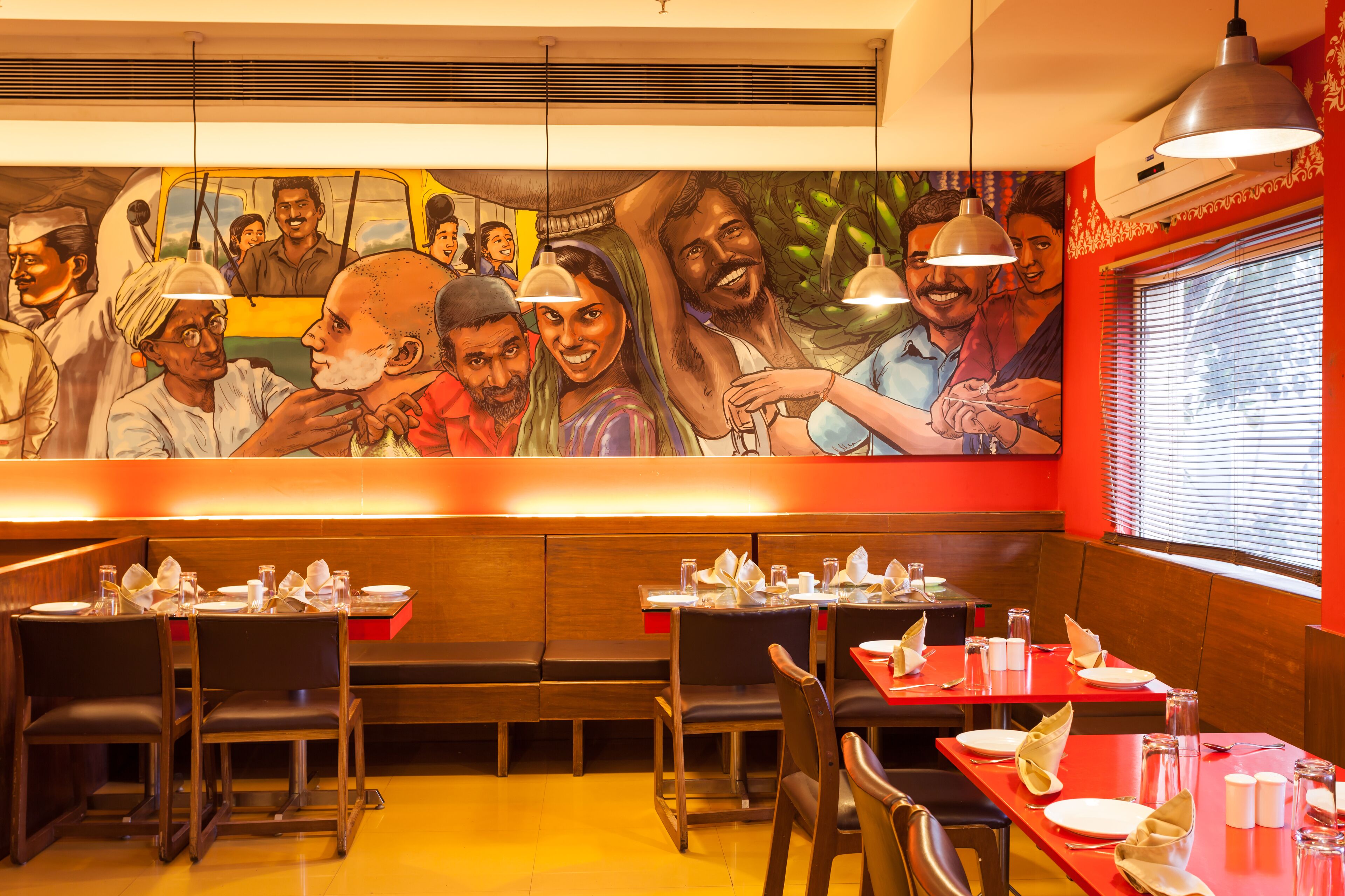 A restaurant with wooden booths, red tables, and a mural depicting a group of people.