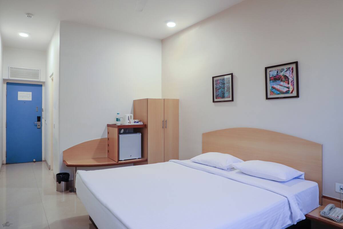 A hotel room with a bed, a desk with a computer, a wardrobe, and two framed pictures on the wall.