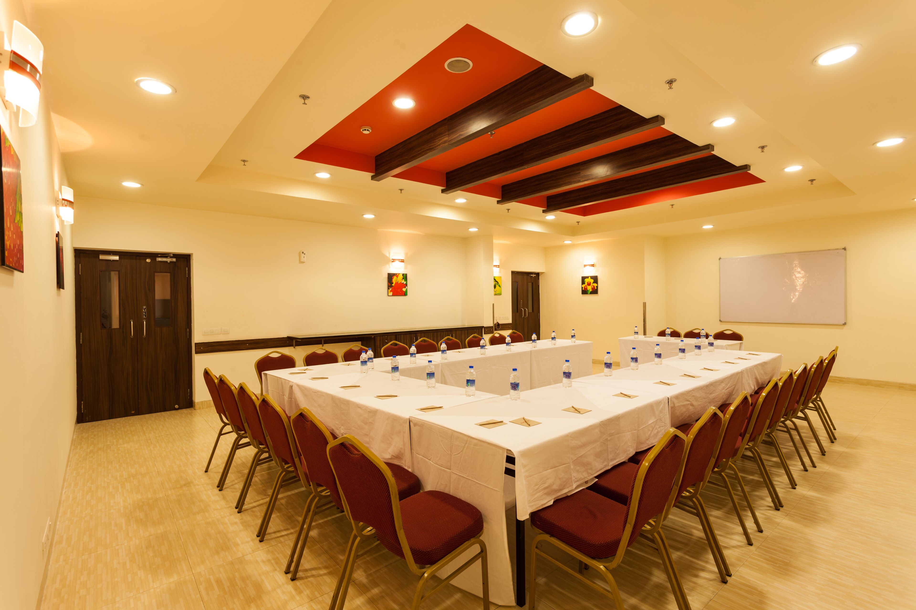 A conference room with a long table, red chairs, and a whiteboard on the wall.