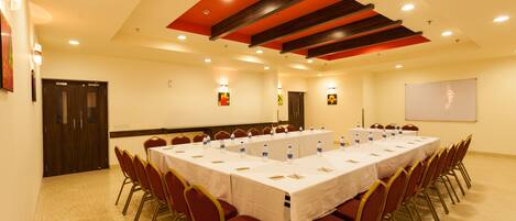 A conference room with a long table, red chairs, and a whiteboard on the wall.