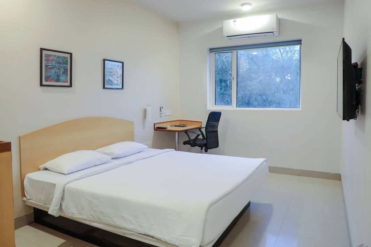 A hotel room with a bed, a desk, a chair, and two framed pictures on the wall.