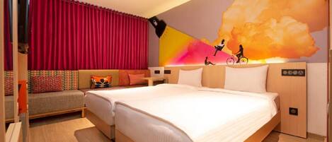 A hotel room with a bed, a sofa, a TV, and a wall mural.