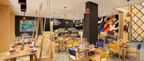 Un restaurante con mesas y sillas de madera, luces colgantes y un mural colorido en la pared.