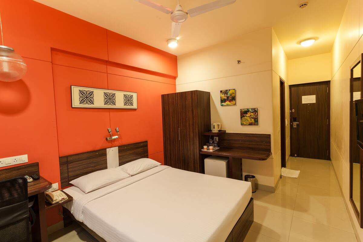 A hotel room with a bed, a desk, a wardrobe, and a small kitchenette.
