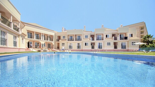 A swimming pool surrounded by multi-story buildings with balconies, a clear sky, and a well-maintained lawn. - Aqua Mar Albufeira (Albufeira)