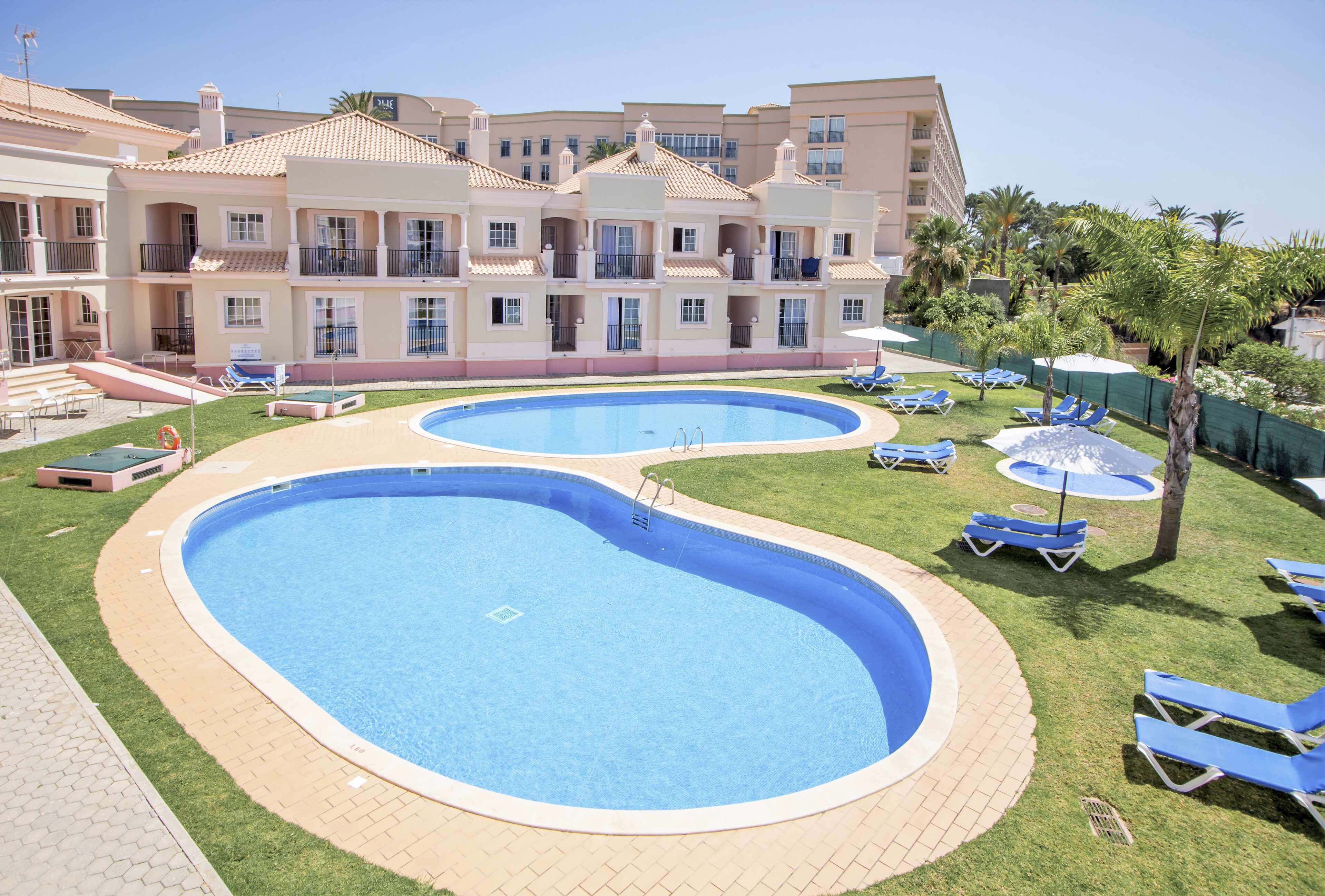 A hotel with a swimming pool, lounge chairs, and a well-maintained lawn.