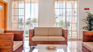 A modern hotel lobby with a beige sofa, wooden furniture, and large windows with curtains. - Aqua Mar Albufeira (Albufeira)
