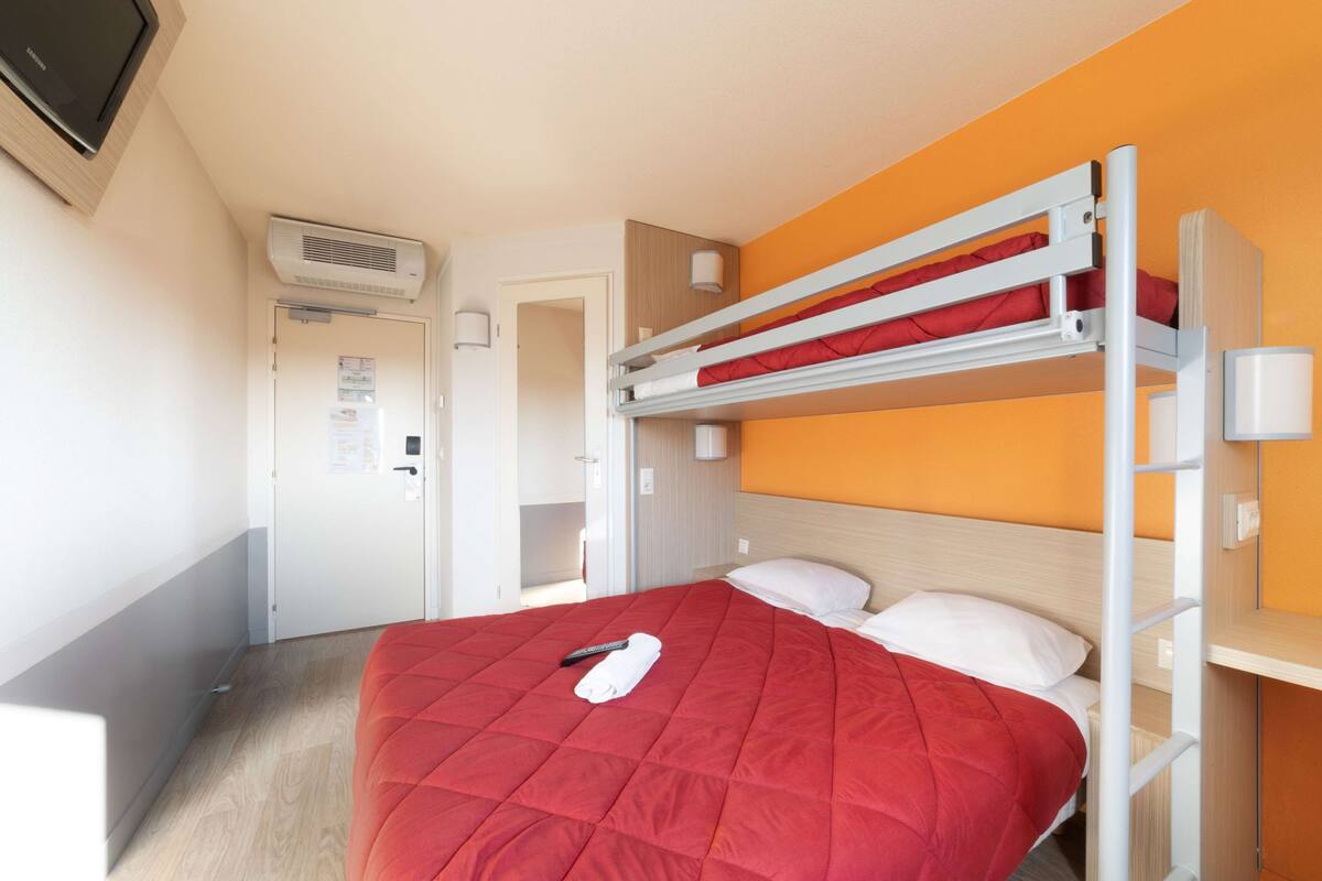 Una cama litera con un edredón rojo, un control remoto y una toalla blanca sobre la cama.