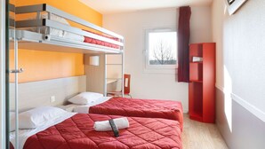 Habitación de hotel con literas, una colcha roja, un televisor montado en la pared y una ventana con vista a árboles.