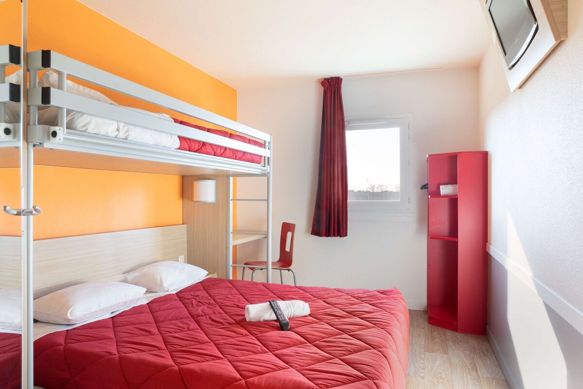 A room with a bunk bed, a red bedspread, a chair, a TV, and a wardrobe.