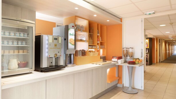 Un área de cocina moderna con un refrigerador, máquina de café y una encimera con diversos alimentos y utensilios de cocina.
