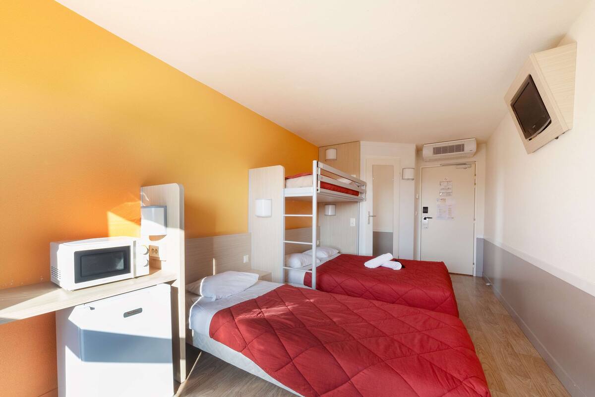 Habitación de hotel con literas, microondas, un pequeño escritorio y una puerta con un cartel.