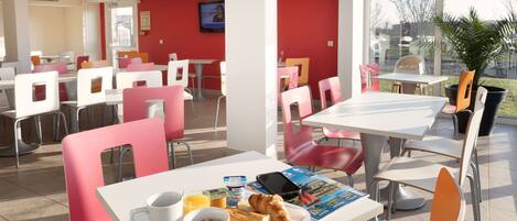 A modern dining area with white tables and chairs, a television on the wall, and a view of the outside.