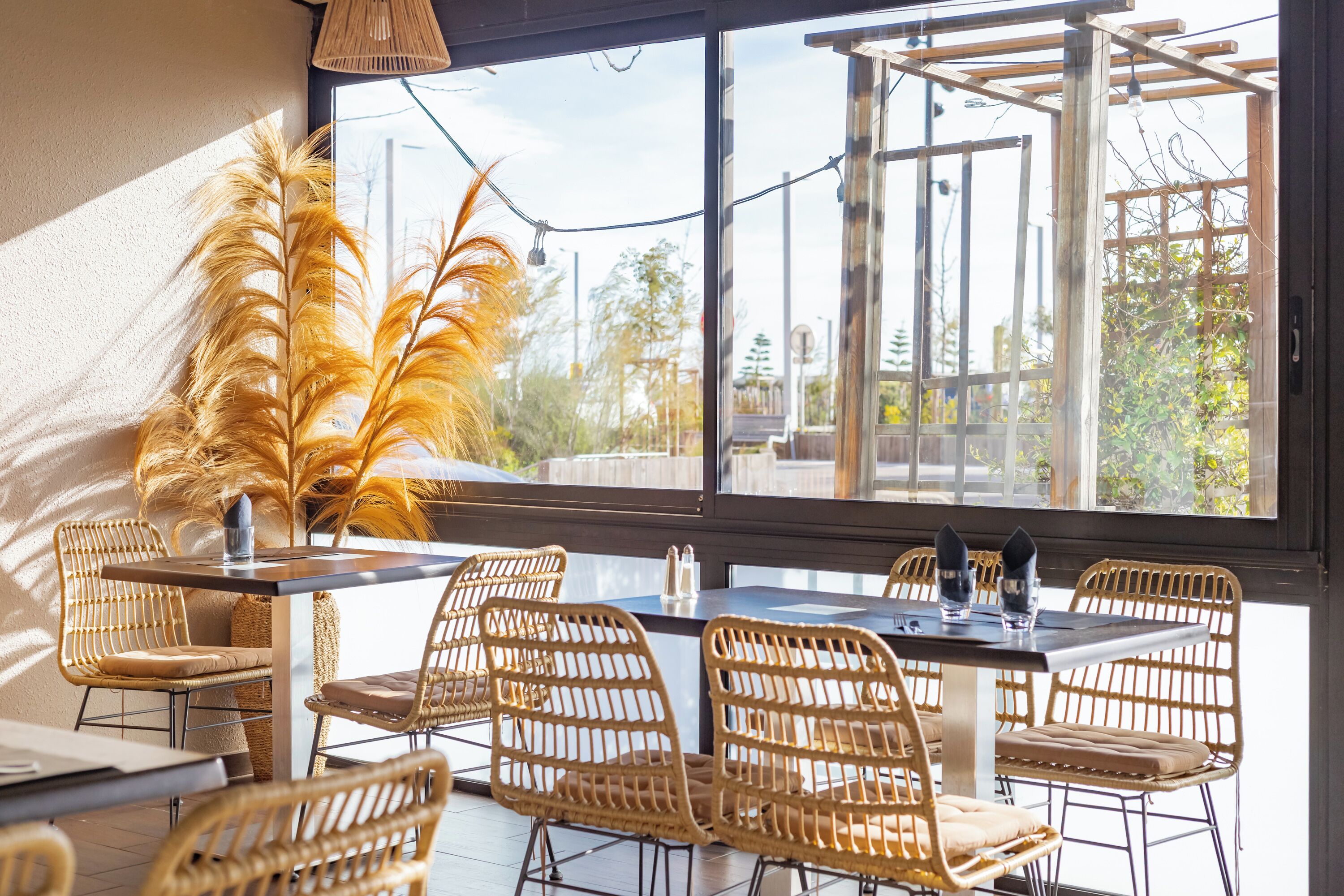 A dining area with wicker chairs, a table, and a large window with a view of trees and a wooden pergola.